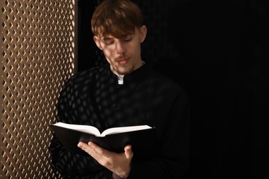 Photo of Catholic priest with Bible near wooden window in confessional. Space for text