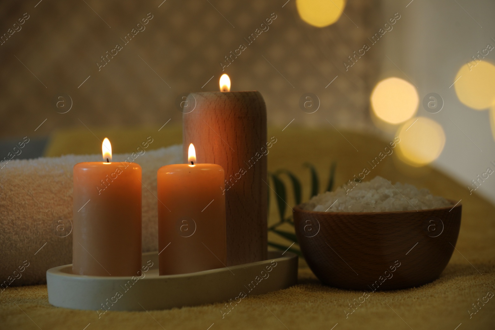 Photo of Spa composition. Burning candles, sea salt and towel on soft yellow surface