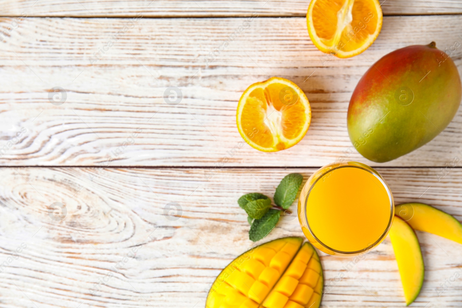 Photo of Glass with fresh mango juice and tasty fruits on wooden table, flat lay. Space for text