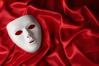 Photo of White theatre mask on red fabric, top view. Space for text