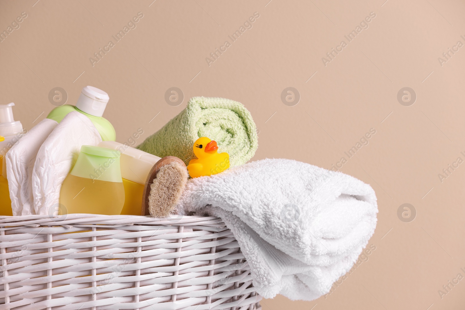 Photo of Wicker basket with baby cosmetic products, bath accessories and rubber duck on beige background, closeup