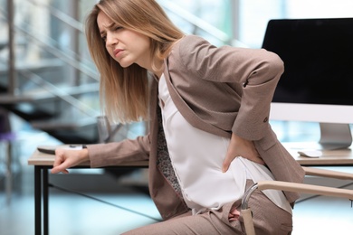 Photo of Young woman suffering from back pain in office