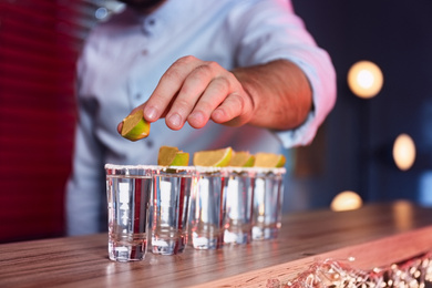 Photo of Barman putting lime on shot glass of Mexican Tequila at bar counter, closeup