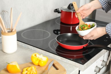 Photo of Woman putting tasty vegetable mix in frying pan at home, closeup