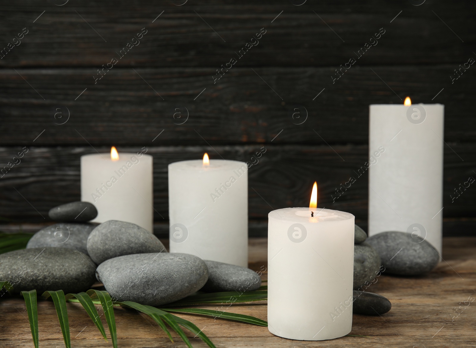 Photo of Burning candles, spa stones and palm leaf on wooden table