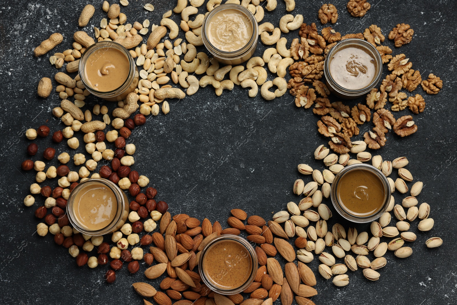 Photo of Frame of tasty nut butters in jars and raw nuts on dark gray table, flat lay. Space for text