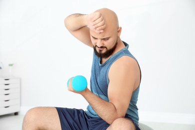 Overweight man doing exercise with dumbbell in gym