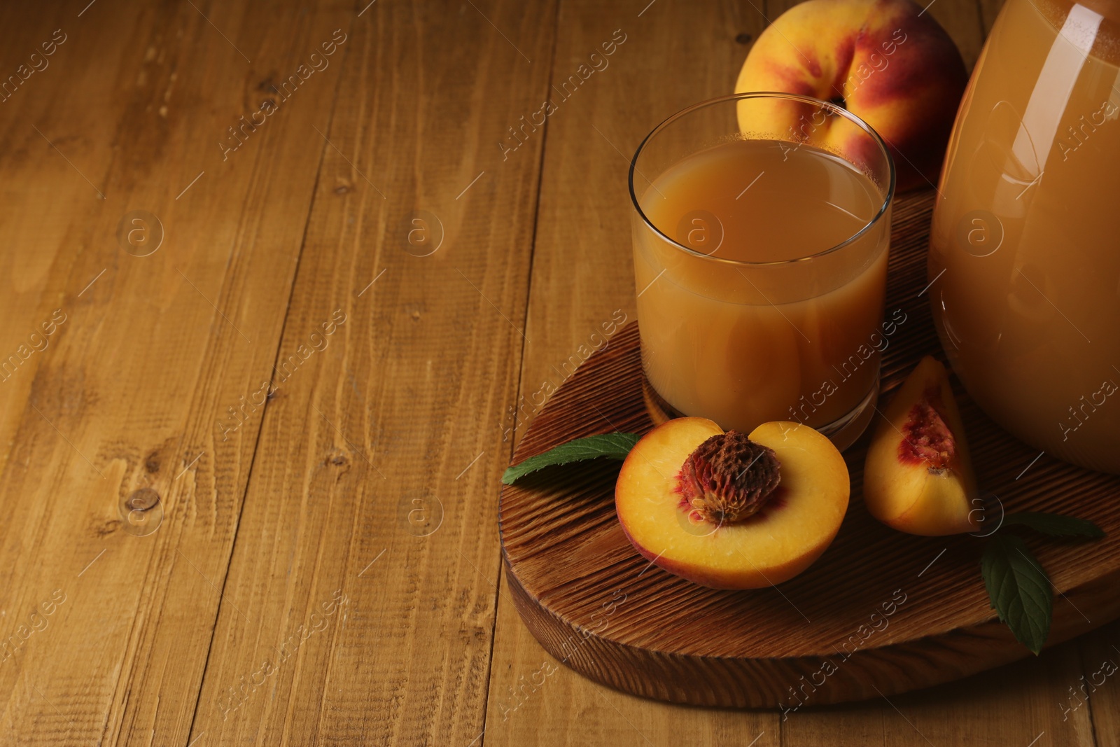 Photo of Delicious peach juice, fresh fruits and leaves on wooden table. Space for text