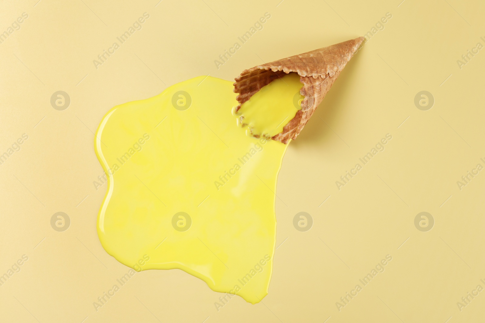 Photo of Melted ice cream and wafer cone on yellow background, above view