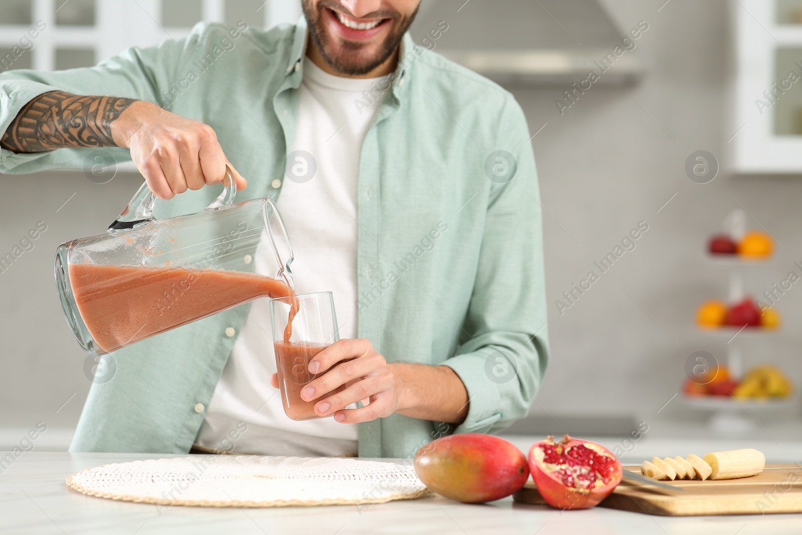 Photo of Man pouring tasty smoothie into glass at white marble table in kitchen, closeup