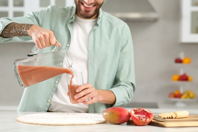 Man pouring tasty smoothie into glass at white marble table in kitchen, closeup