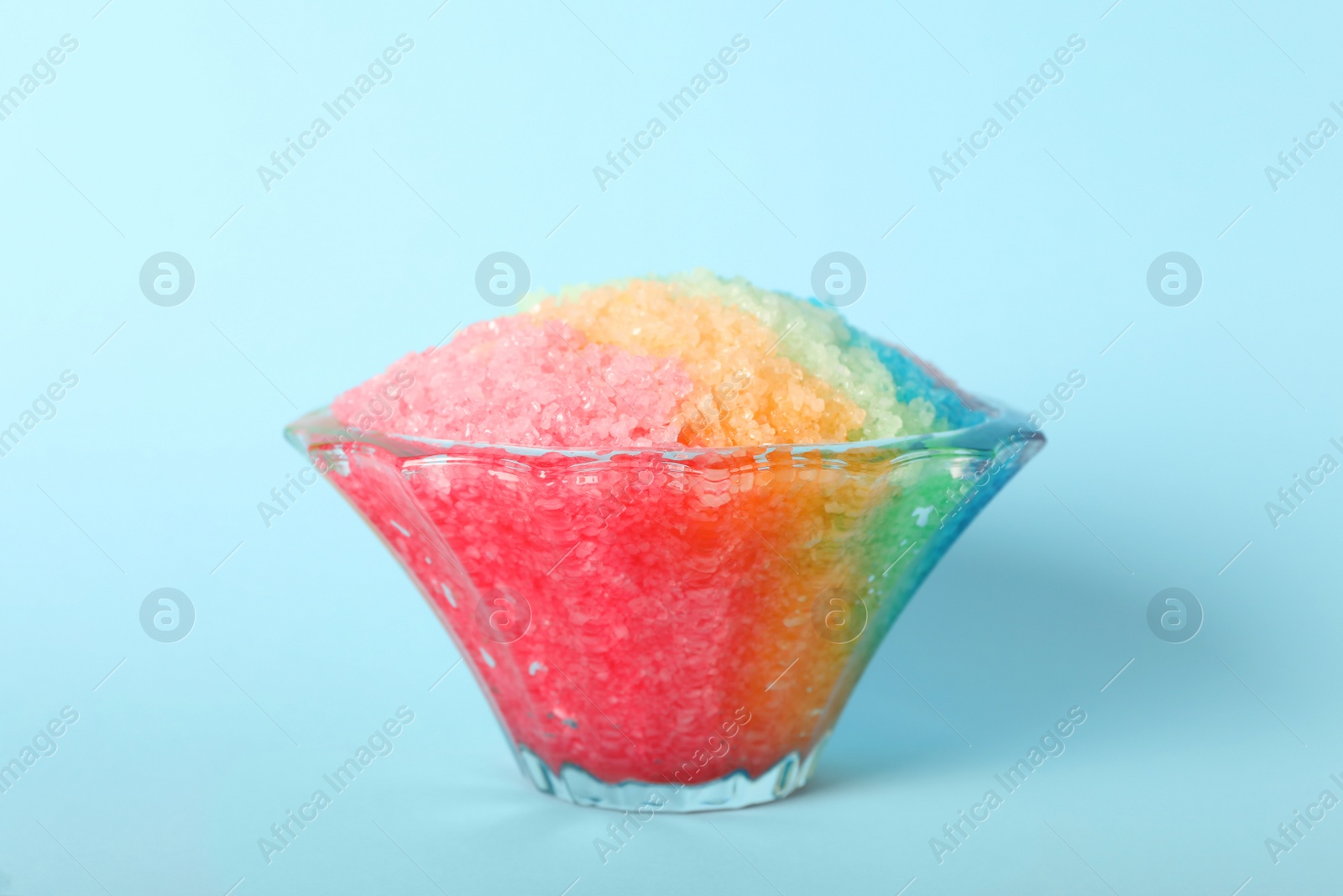 Photo of Rainbow shaving ice in glass dessert bowl on light blue background