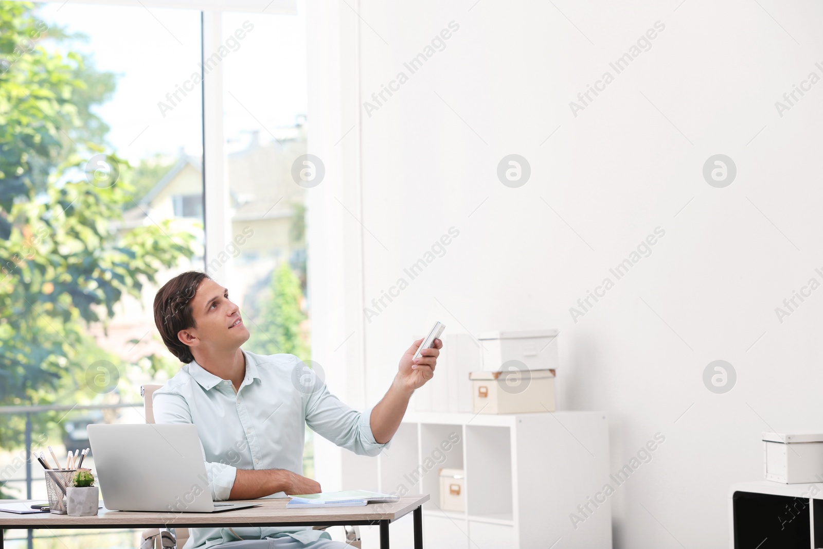 Photo of Young man with air conditioner remote in office