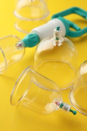 Plastic cups and hand pump on yellow background, closeup. Cupping therapy