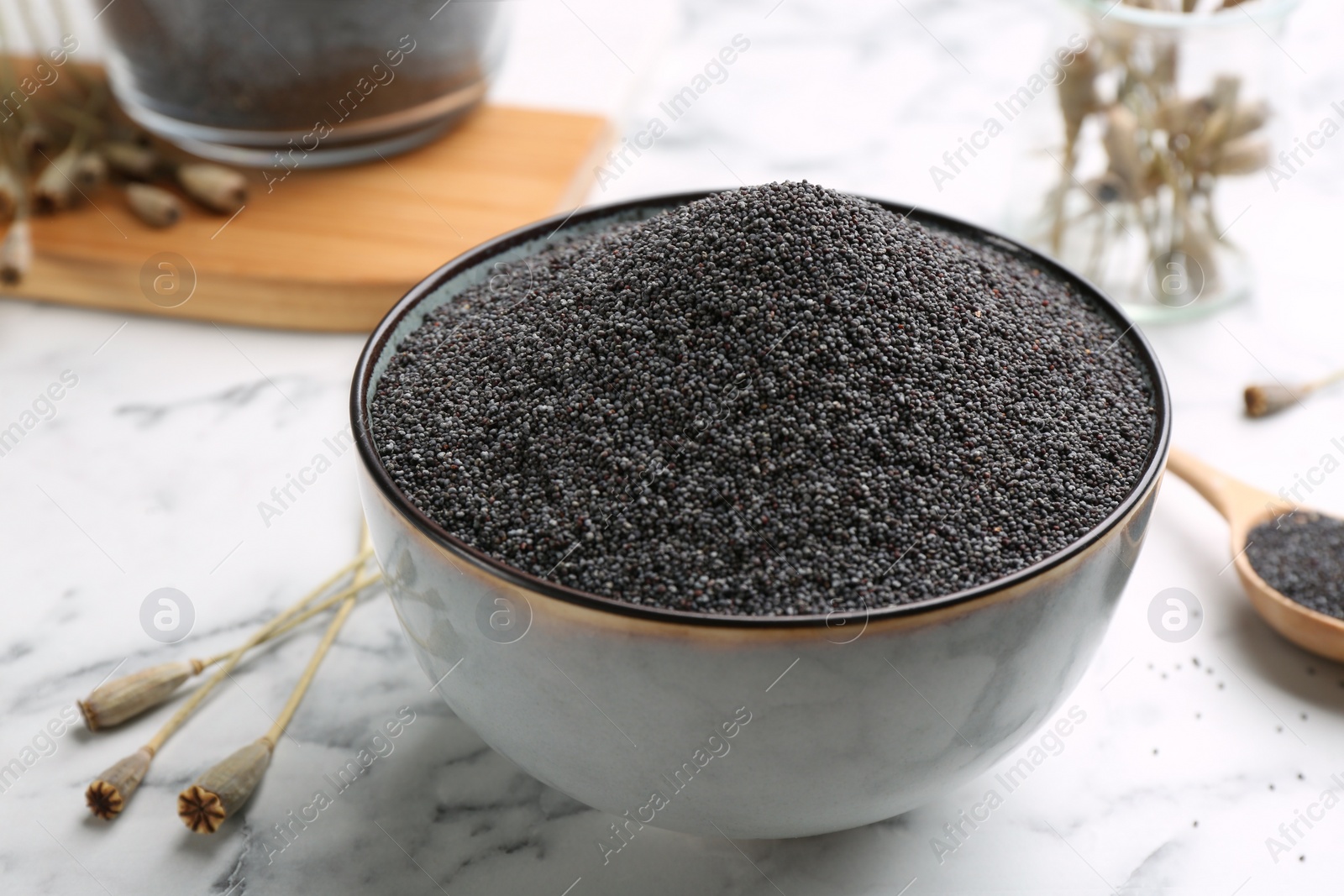 Photo of Dried poppyheads and bowl with seeds on white marble table