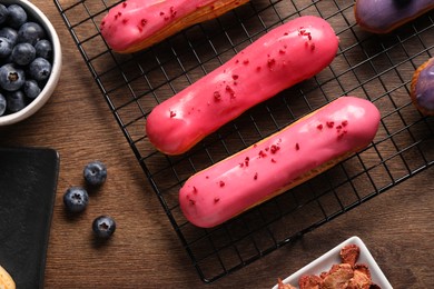 Tasty glazed eclairs and blueberries on wooden table, flat lay