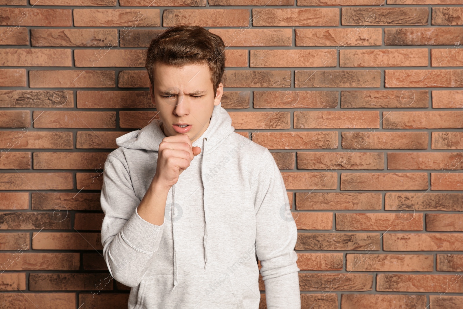 Photo of Teenage boy suffering from cough near brick wall. Space for text
