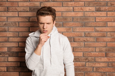 Teenage boy suffering from cough near brick wall. Space for text
