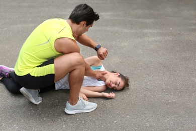 Young man checking pulse of unconscious woman on street