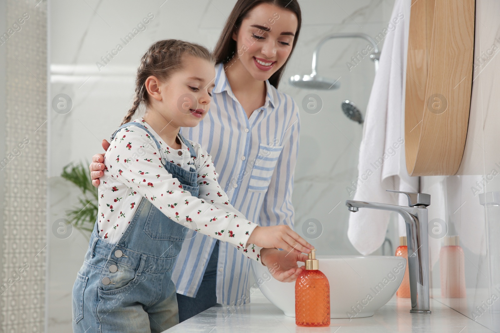 Photo of Mother and daughter washing hands with liquid soap in bathroom