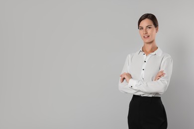 Young secretary with crossed arms on light grey background, space for text