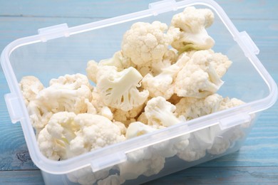 Photo of Plastic container with different fresh cut cauliflower on light blue wooden table, closeup