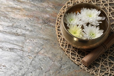 Photo of Tibetan singing bowl with water, beautiful chrysanthemum flowers and mallet on table, space for text