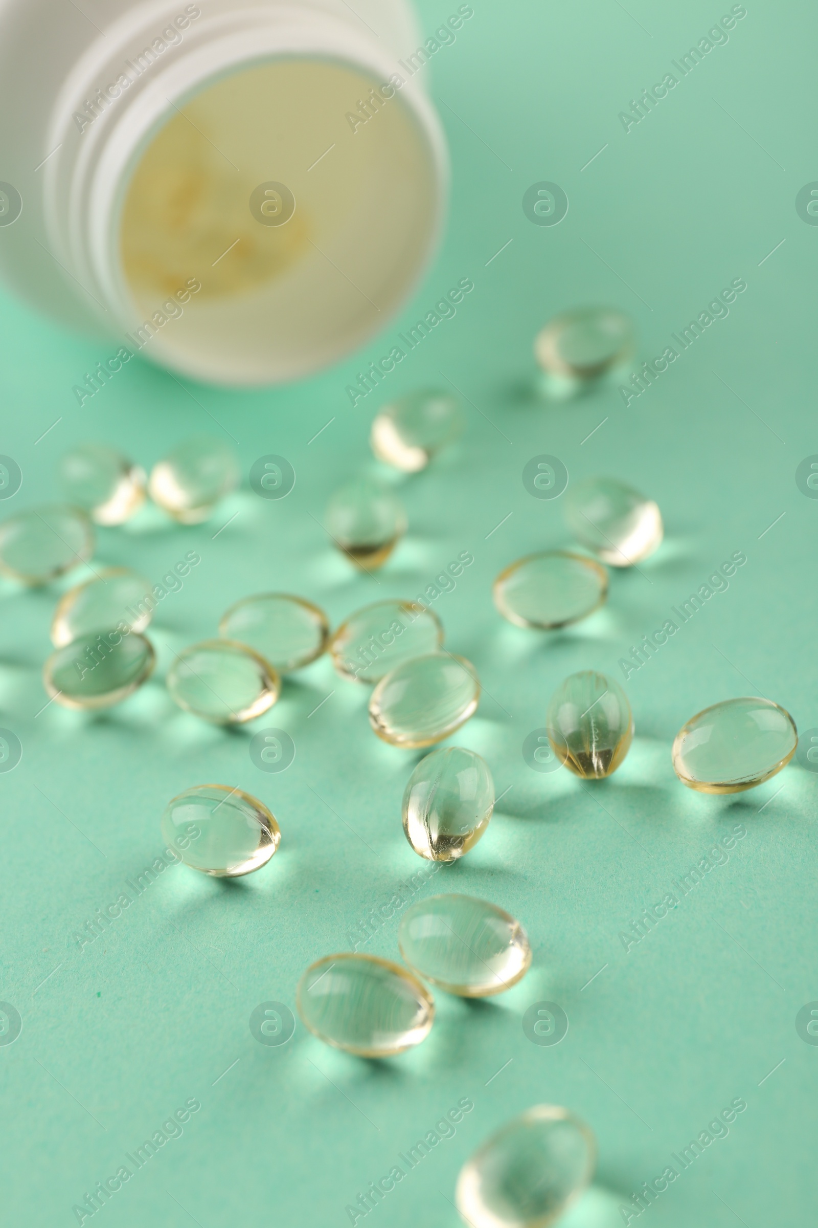 Photo of Bottle and vitamin capsules on turquoise background, closeup