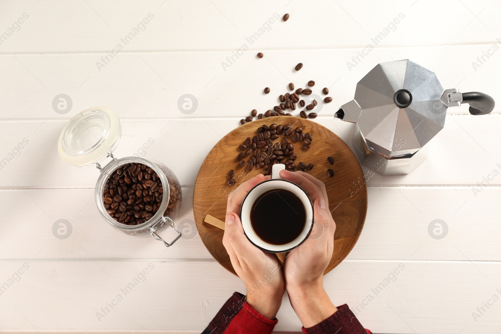 Photo of Man with cup of aromatic brewed coffee, top view. Moka pot and beans on white wooden table