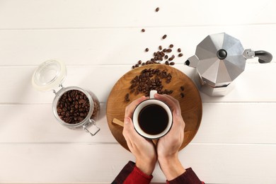 Man with cup of aromatic brewed coffee, top view. Moka pot and beans on white wooden table