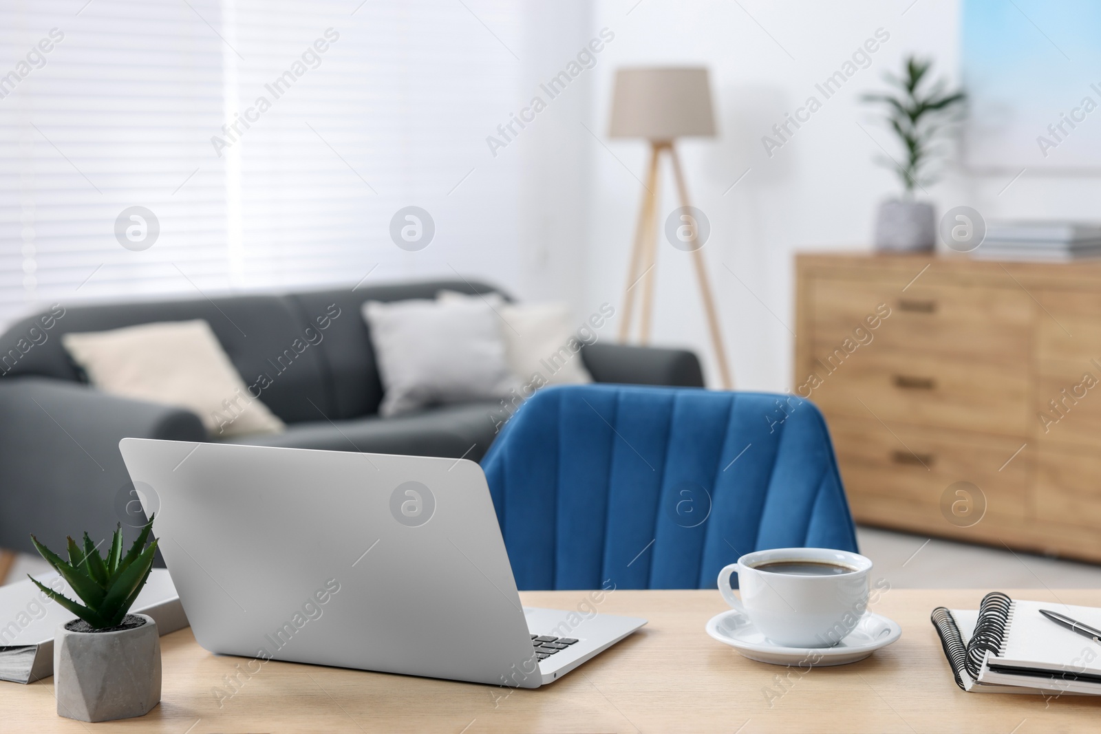 Photo of Home workspace. Laptop, cup of coffee and stationery on wooden desk indoors