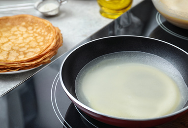 Photo of Delicious thin pancake in frying pan on induction stove, closeup