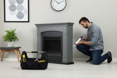 Photo of Man sealing electric fireplace with caulk near wall in room