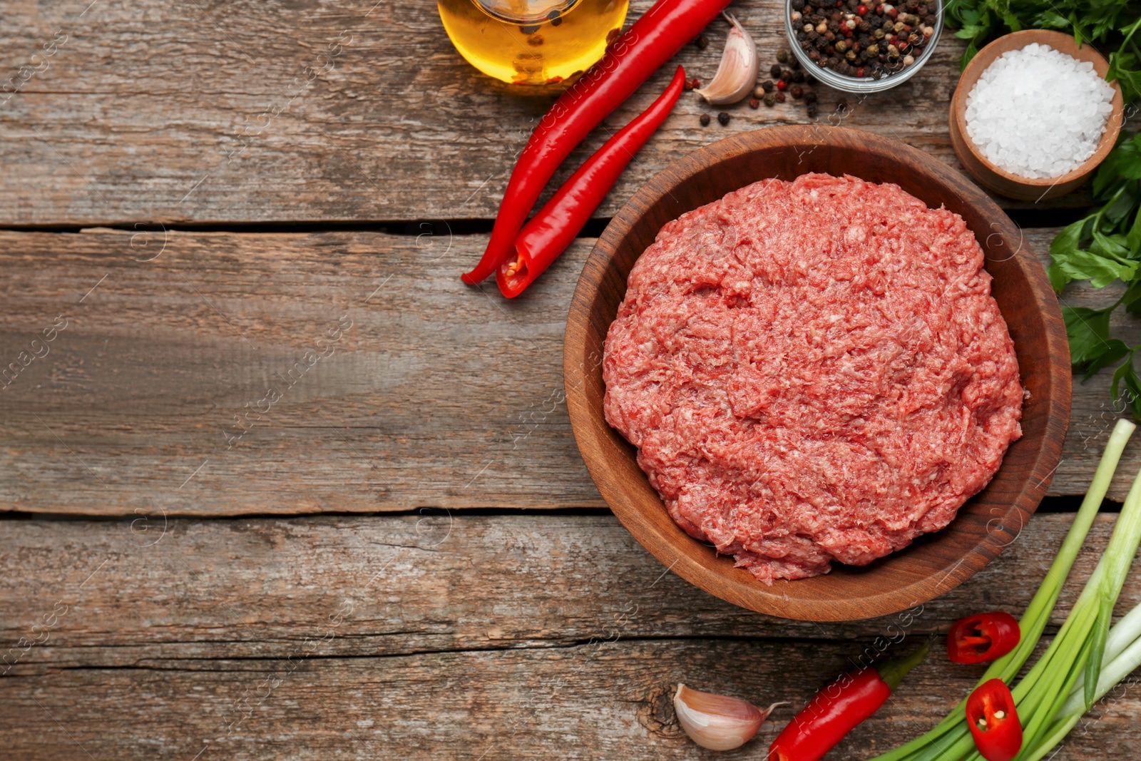Photo of Bowl with raw fresh minced meat and ingredients on wooden table, flat lay. Space for text