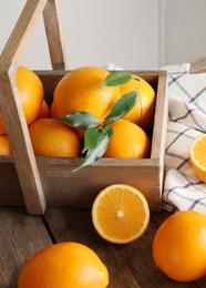 Fresh oranges with leaves and rustic box on wooden table