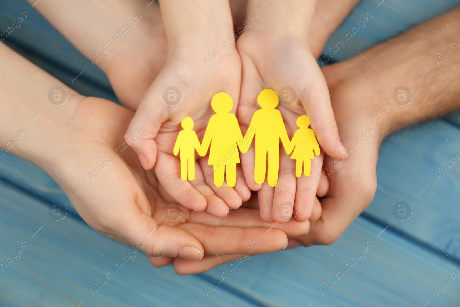 Photo of Parents and kid holding paper cutout of family in hands at turquoise wooden table, top view