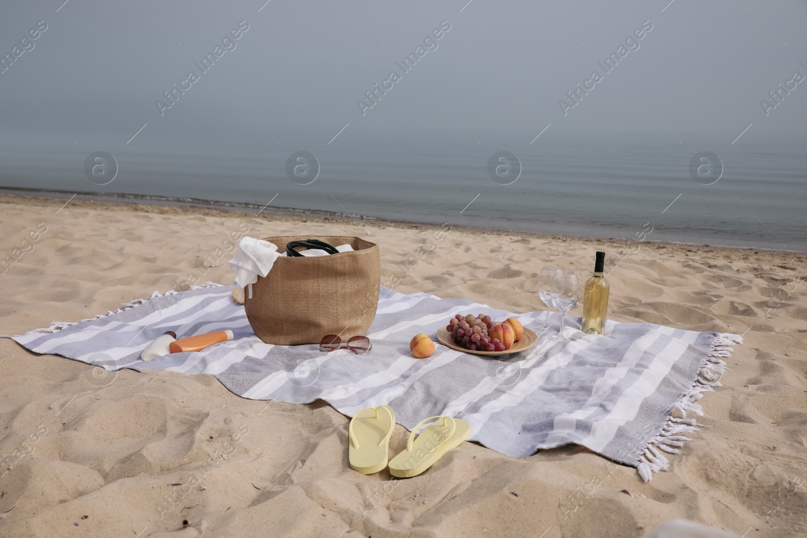 Photo of Bag, blanket, wine and other stuff for beach picnic on sandy seashore