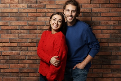 Young couple in warm sweaters near brick wall