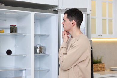 Photo of Thoughtful man near empty refrigerator in kitchen