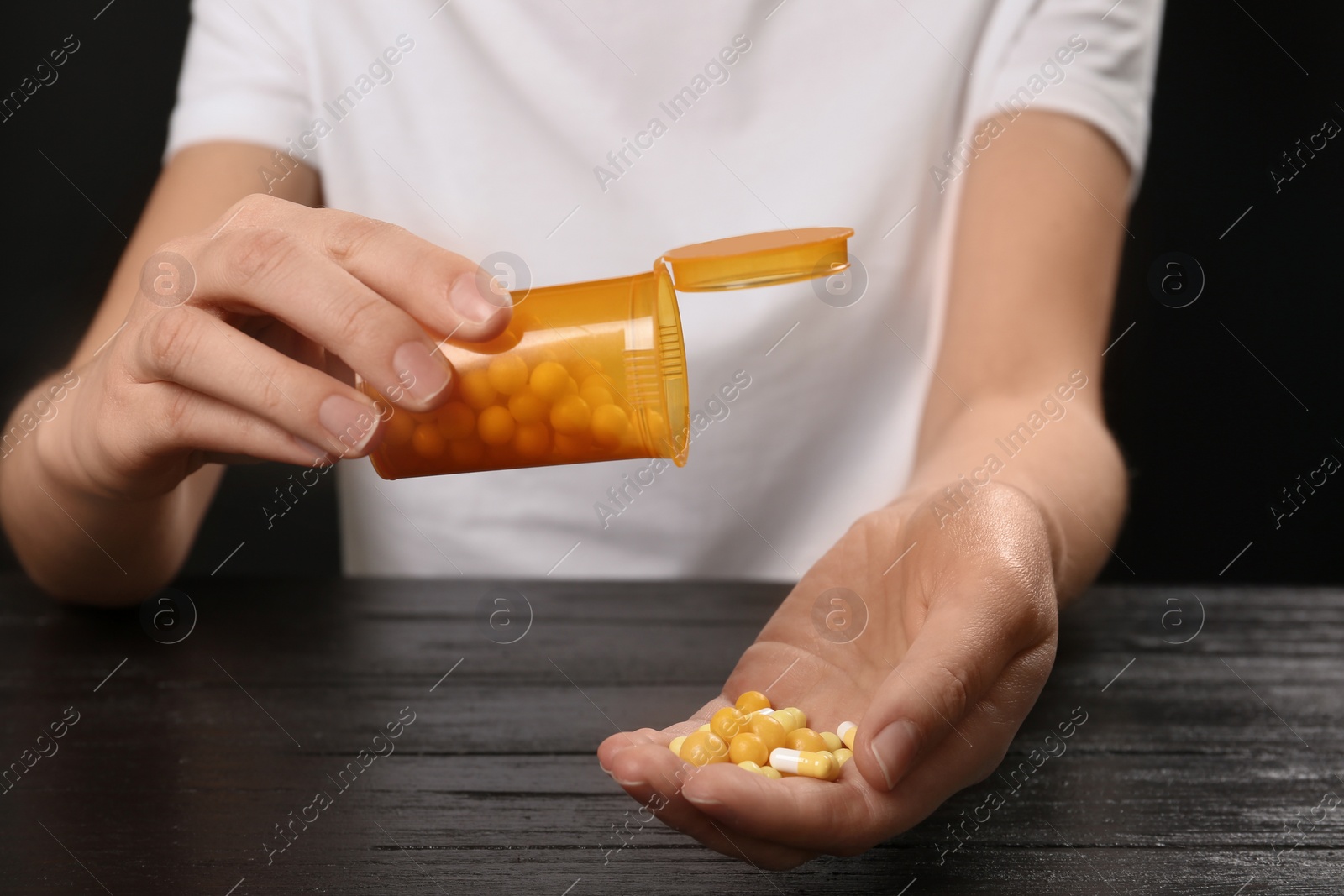 Photo of Woman pouring pills out of bottle into hand at table, closeup