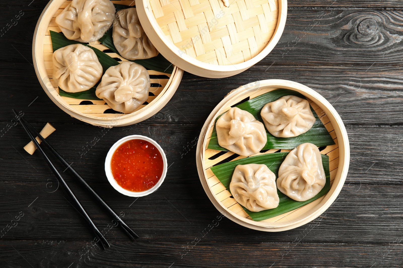 Photo of Bamboo steamers with tasty baozi dumplings, chopsticks and bowl of sauce on wooden background, top view