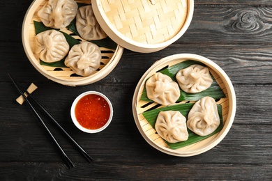 Bamboo steamers with tasty baozi dumplings, chopsticks and bowl of sauce on wooden background, top view