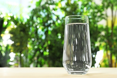 Photo of Glass of water on table against blurred background, space for text. Refreshing drink