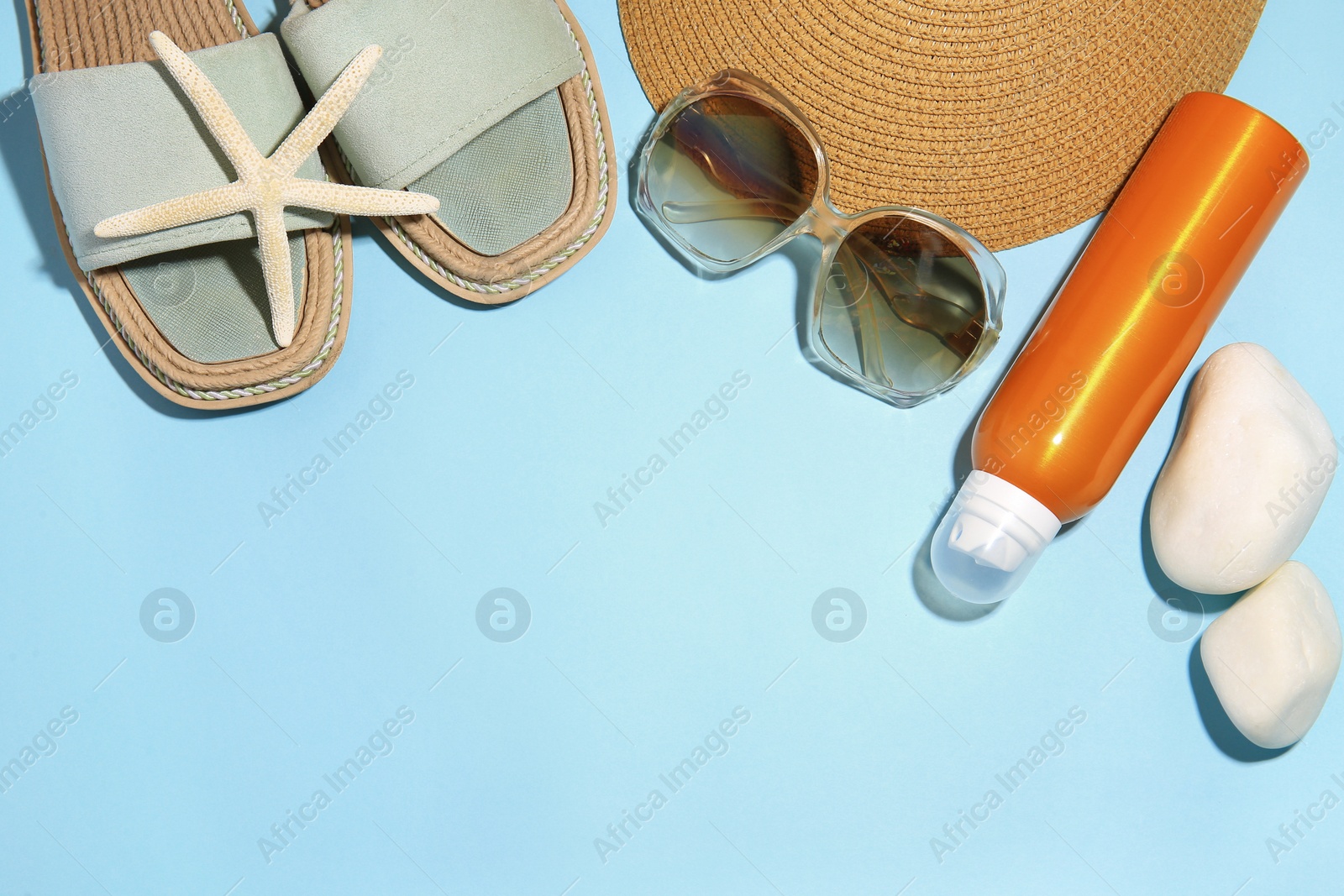 Photo of Sunscreen, starfish, stones and beach accessories on light blue background, flat lay and space for text. Sun protection