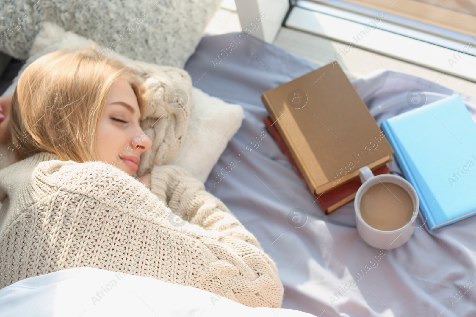 Photo of Beautiful young woman sleeping near books and cup of coffee at home, top view.  Winter atmosphere