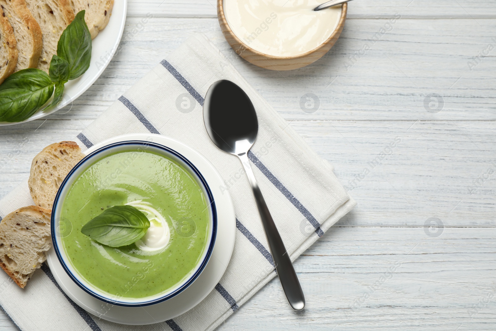 Photo of Tasty homemade zucchini cream soup served on white wooden table, flat lay