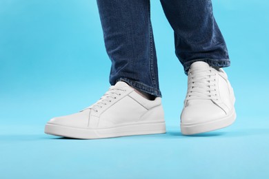 Photo of Man wearing stylish white sneakers on light blue background, closeup