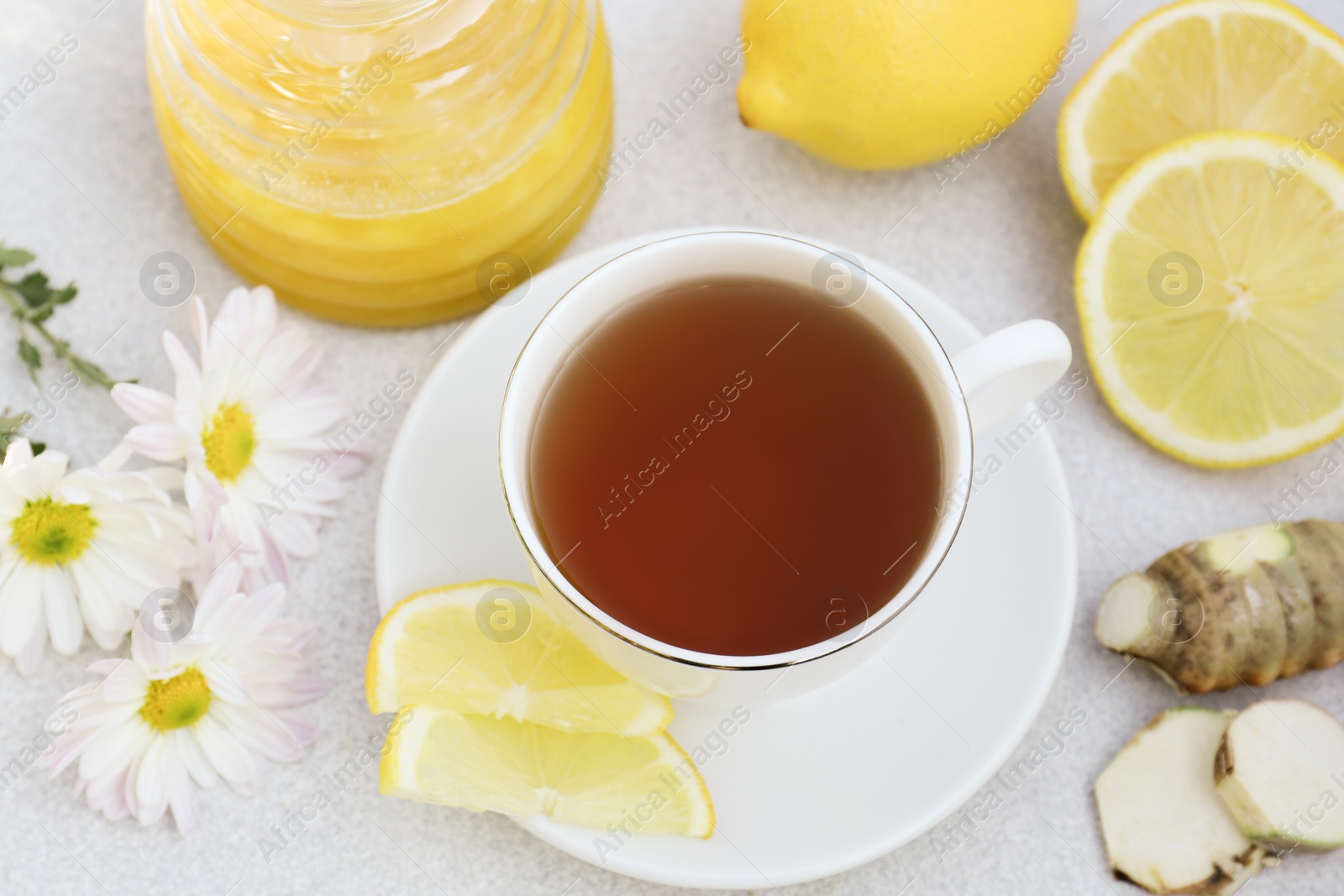 Photo of Cup of delicious tea with honey, lemon and ginger on white table, above view