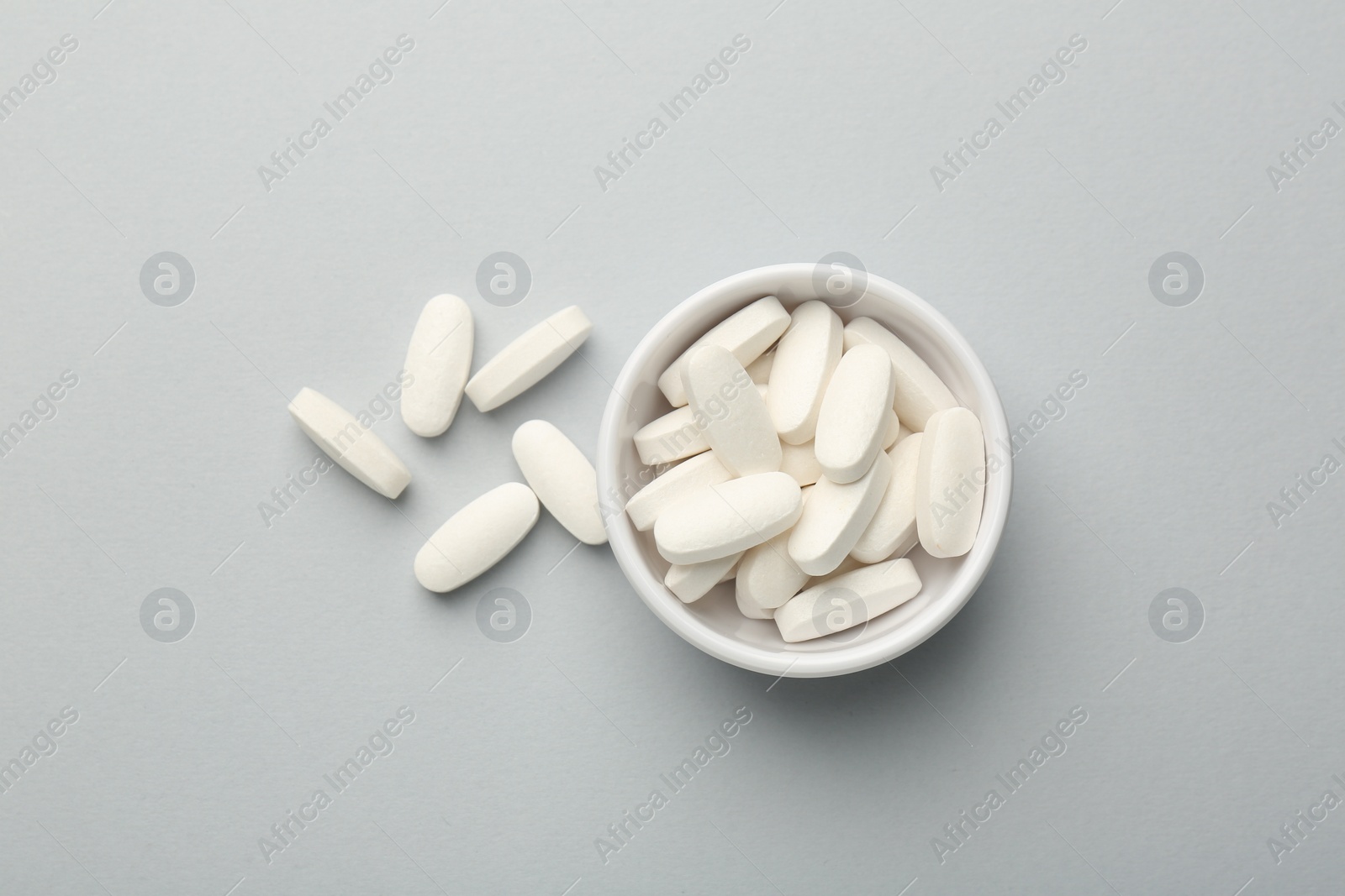 Photo of Vitamin pills in bowl on grey background, top view