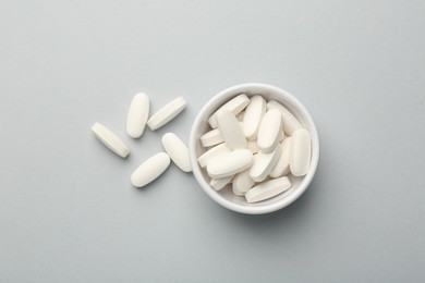 Vitamin pills in bowl on grey background, top view